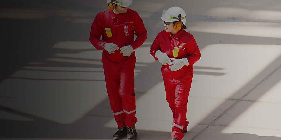 Karyawan pria dan wanita berjalan dengan mengenakan seragam overal merah dengan helm putih serta alat pelindung pendengaran
