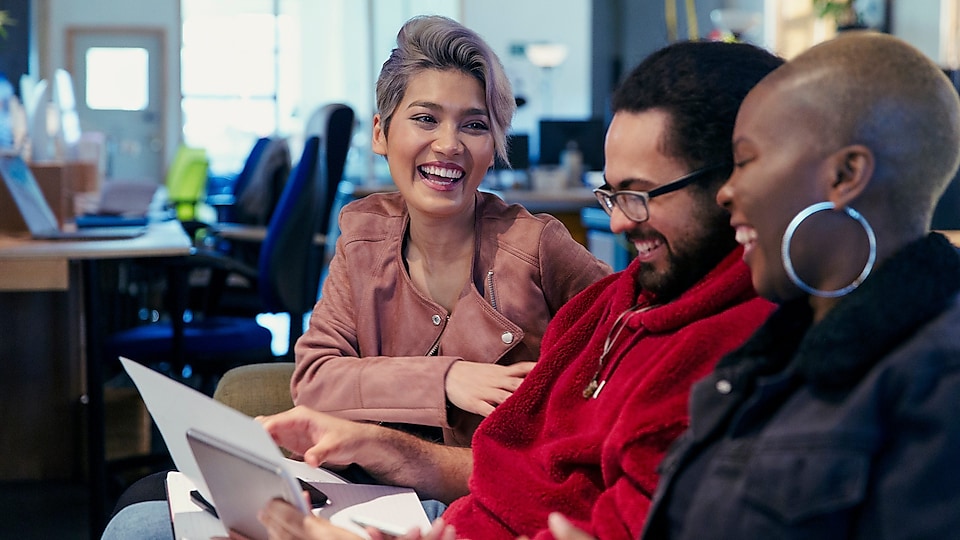 Three people in an office sitting together, looking at papers and laughing