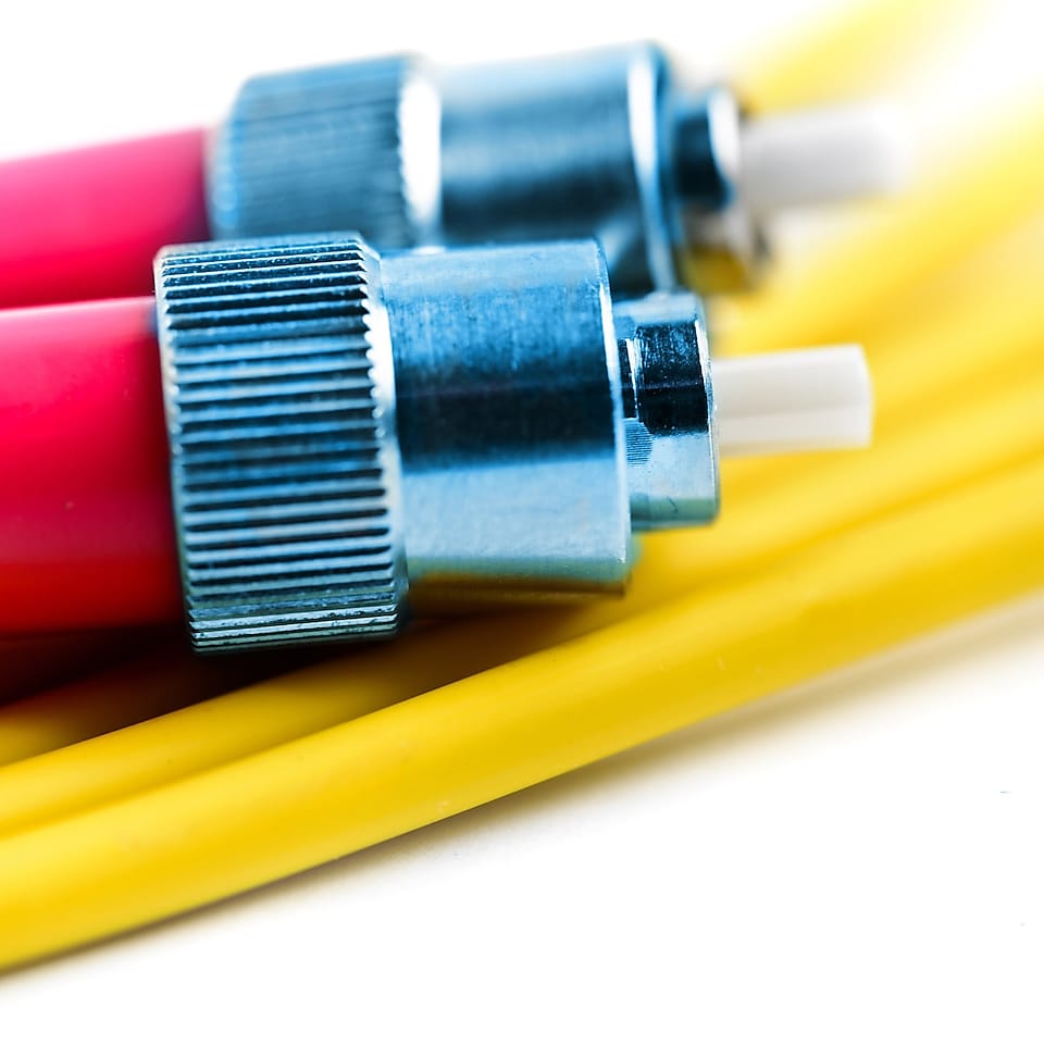 Dua ujung konektor dari tautan kabel optik tergeletak di atas kabel kuning
