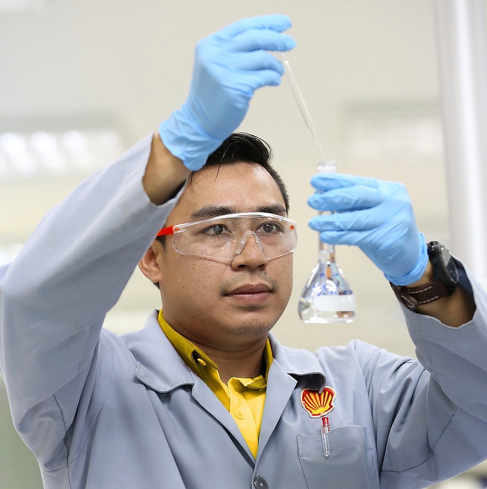 Ilmuwan Shell memakai kacamata pelindung meneteskan cairan dari pipet ke dalam gelas kimia