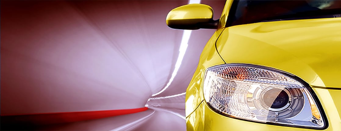 Bagian depan mobil kuning melintasi terowongan, lampu depan kanan dan kaca samping terlihat.