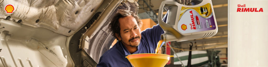 Seorang mekanik sedang menuang pelumas Shell Rimula R4 Plus ke dalam mesin truk berat.