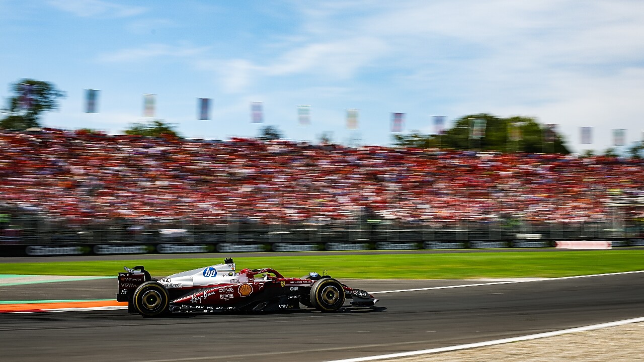 Mobil balap tim Scuderia Ferrari HP di sirkuit berlatar belakang penonton di tribun.