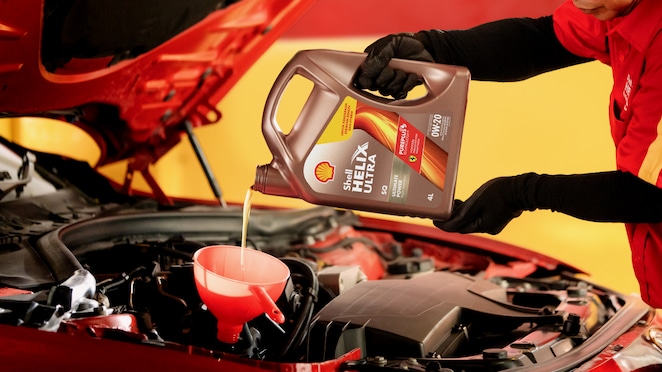 Seorang mekanik sedang menuang oli Shell Helix Ultra ke dalam mesin mobil.