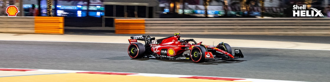 Mobil balap ferrari dengan logo Shell sedang melaju di sirkuit.