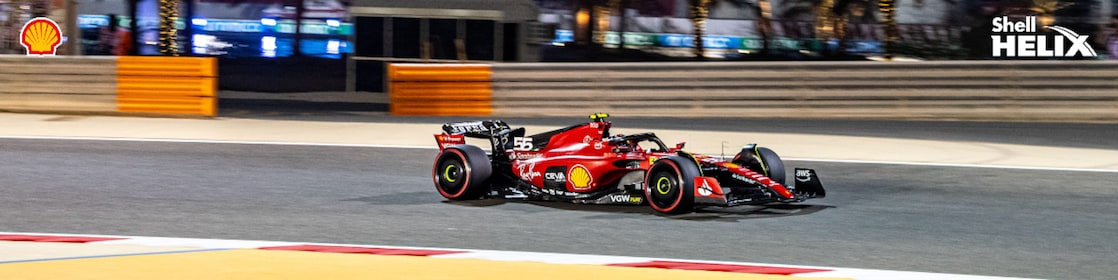 Mobil balap ferrari dengan logo Shell sedang melaju di sirkuit.