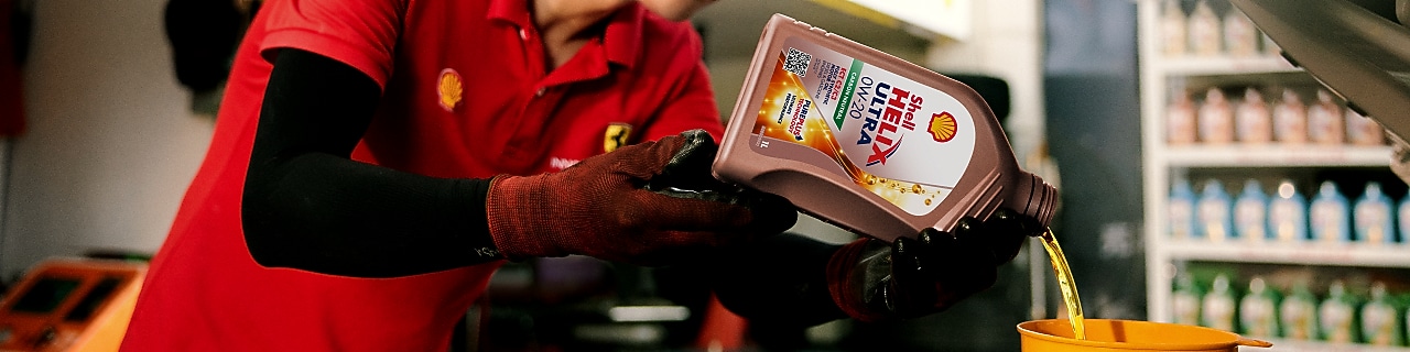 Seorang mekanik sedang menuangkan oli ke dalam mesin mobil