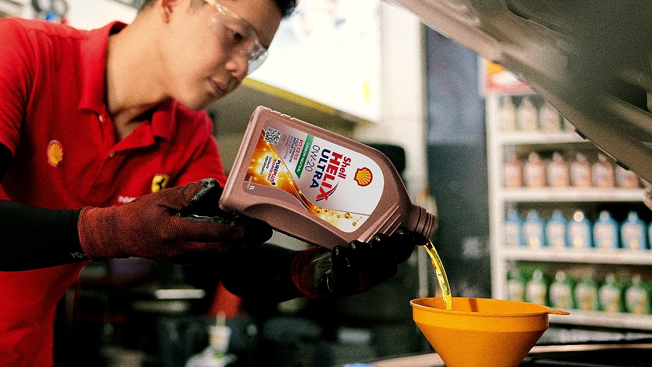 Seorang mekanik sedang menuangkan oli ke dalam mesin mobil.