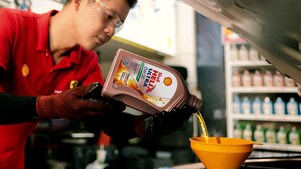 Seorang mekanik sedang menuangkan oli ke dalam mesin mobil.