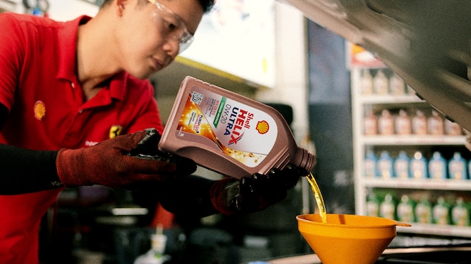 Seorang mekanik sedang menuangkan oli ke dalam mesin mobil.