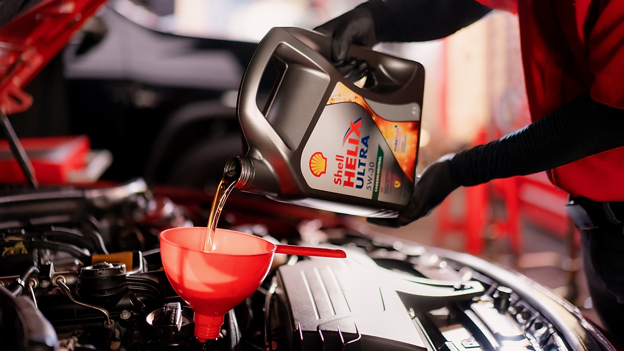 Seorang mekanik sedang menuangkan oli ke dalam mesin mobil.