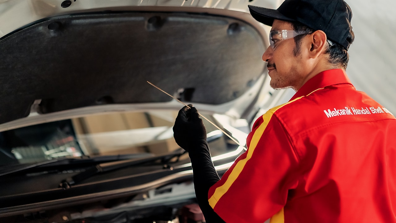 Seorang mekanik sedang memeriksa kondisi pelumas pada mobil.