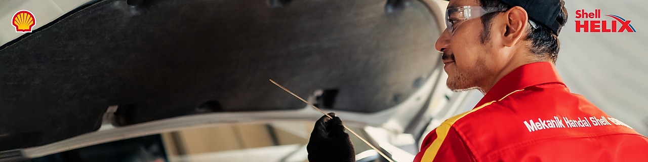 Seorang mekanik Shell sedang memeriksa oli mobil menggunakan dipstick.