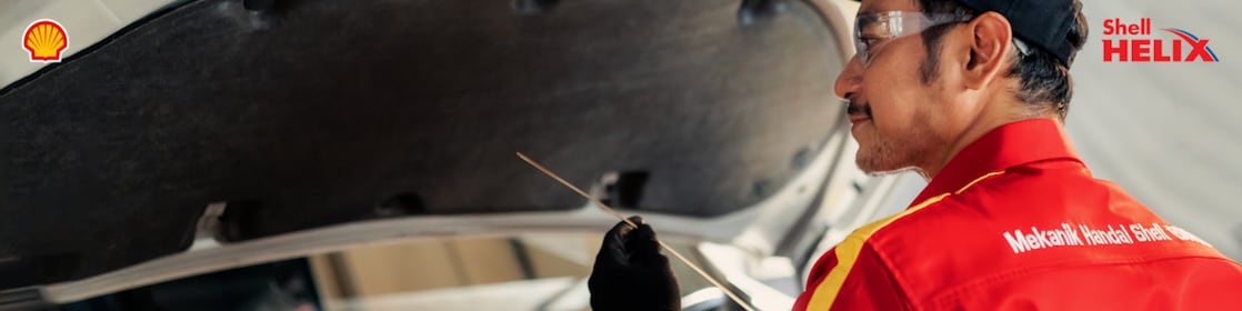Seorang mekanik Shell sedang memeriksa oli mobil menggunakan dipstick.