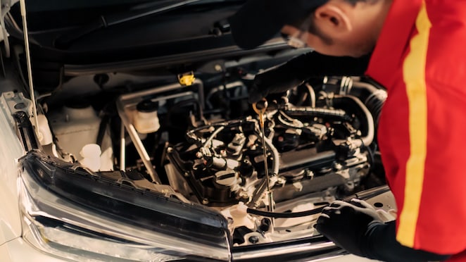 Seorang mekanik Shell sedang memeriksa oli mobil menggunakan dipstick