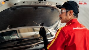 Seorang mekanik Shell sedang memeriksa oli mobil menggunakan dipstick.