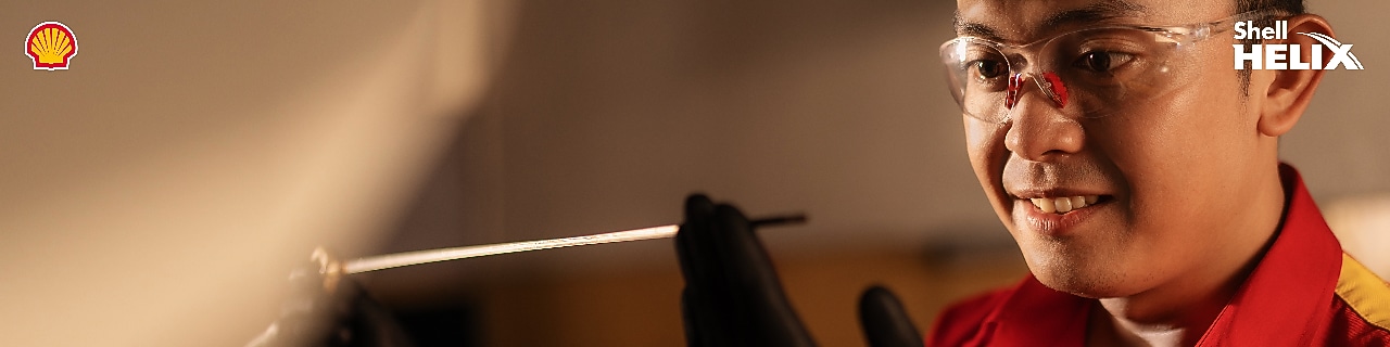 Seorang mekanik Shell sedang melihat dipstick yang digunakan untuk memeriksa kondisi oli mobil.