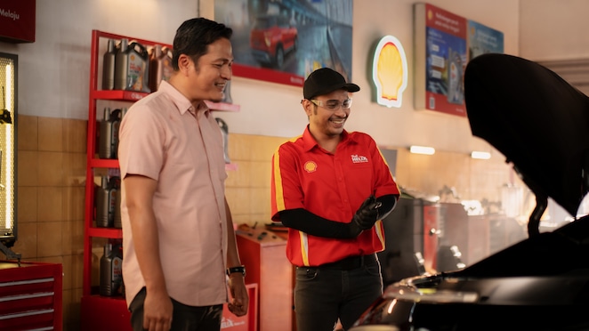 Seorang mekanik sedang mengganti pelumas mesin mobil.