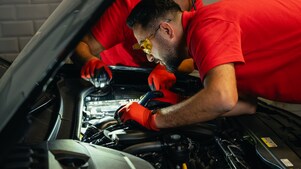 Dua orang mekanik sedang memeriksa mesin mobil dengan teliti