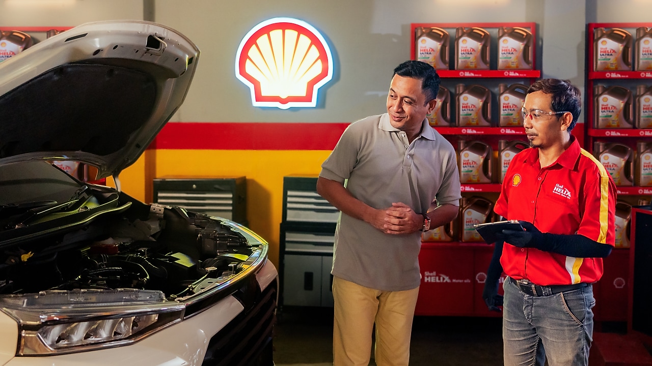 Seorang pria sedang konsultasi dengan mekanik Shell Helix mengenai oli mobilnya di bengkel.