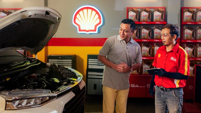 Seorang pria sedang konsultasi dengan mekanik Shell Helix mengenai oli mobilnya di bengkel.