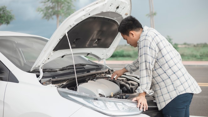 Seorang pria sedang memeriksa mesin mobil yang lama tidak digunakan.