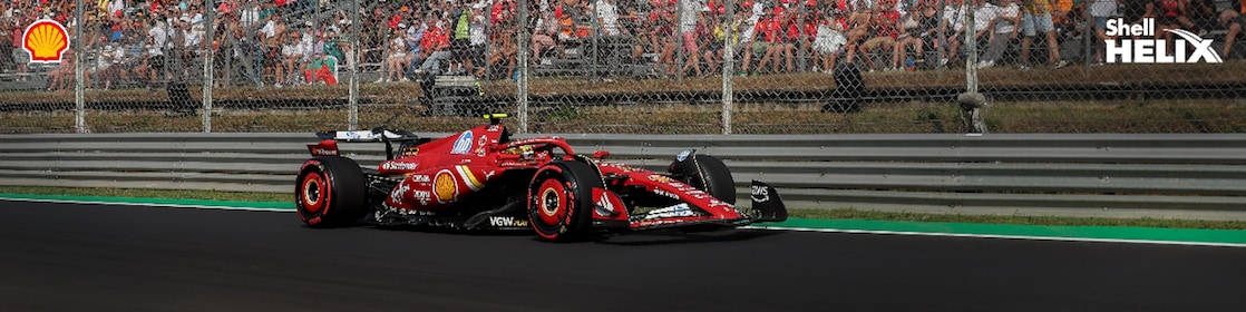 Mobil balap ferrari dengan logo Shell sedang melaju di sirkuit.