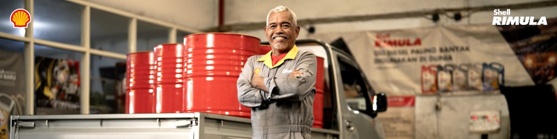 Seorang mekanik sedang berdiri di depan truk pick-up di sebuah bengkel.
