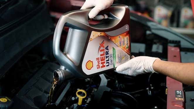 Seorang teknisi sedang mengganti oli mobil dengan Shell Helix.