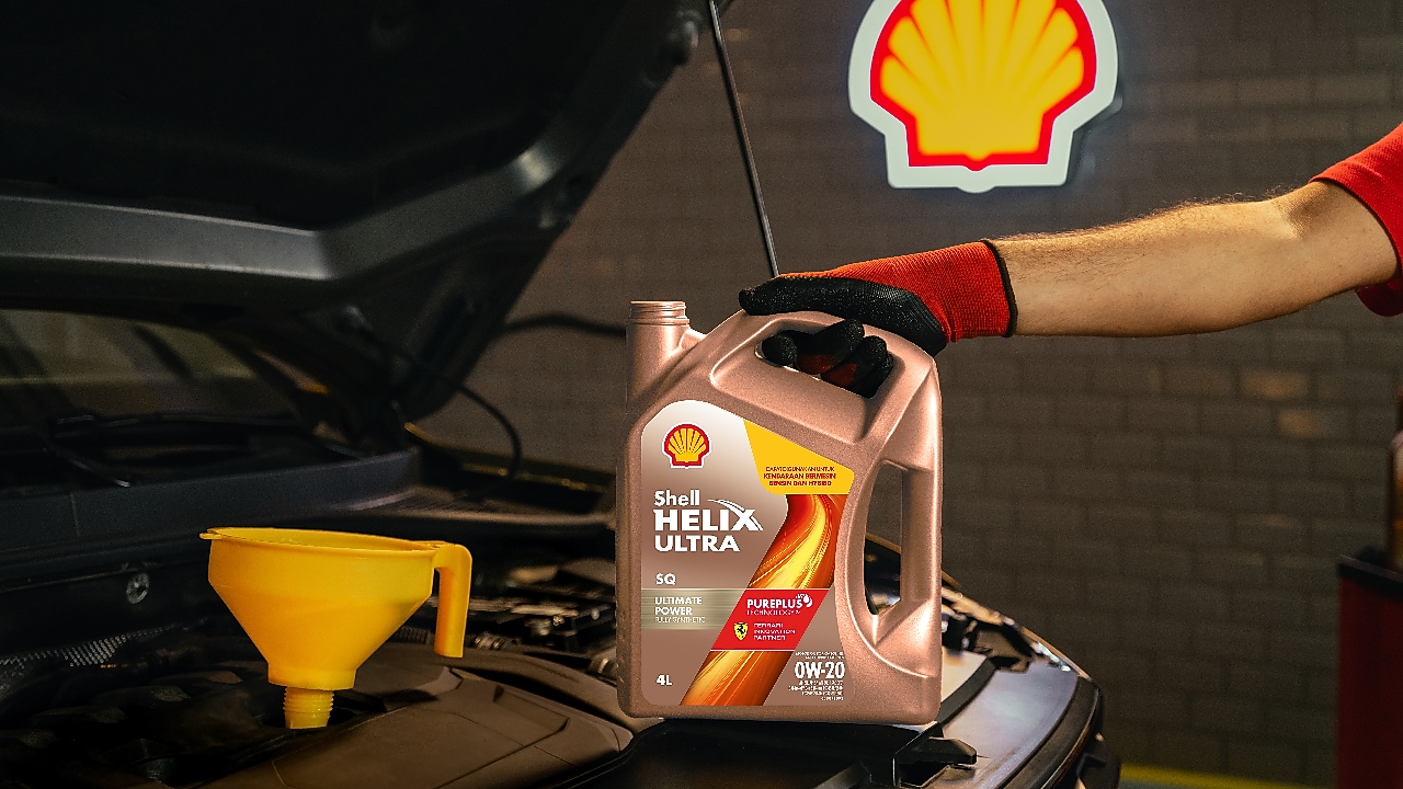 Botol oli Shell Helix Ultra 0W-20 dipegang mekanik di depan mesin mobil