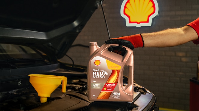 Botol oli Shell Helix Ultra 0W-20 dipegang mekanik di depan mesin mobil