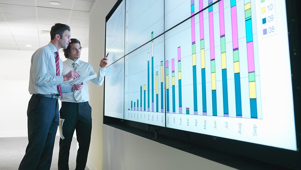 Seorang pebisnis menganalisis laporan yang ditampilkan di layar digital besar