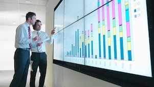 Seorang pebisnis menganalisis laporan yang ditampilkan di layar digital besar